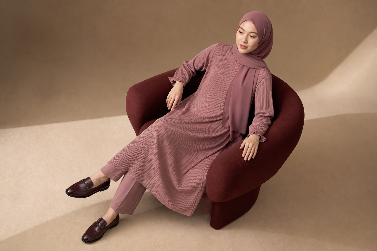 Bordo koltukta pudra tonlarında pilili takım giyen kadın model